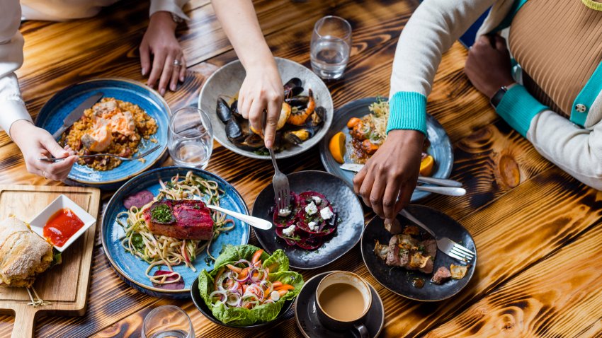 Unrecognisable friends sitting at a wooden table in a modern restaurant,