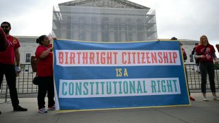 People hold a sign as they participate in a protest outside the U.S. Supreme Court over President Donald Trump’s move to end birthright citizenship as the court hears arguments over the order in Washington, May 15, 2025.